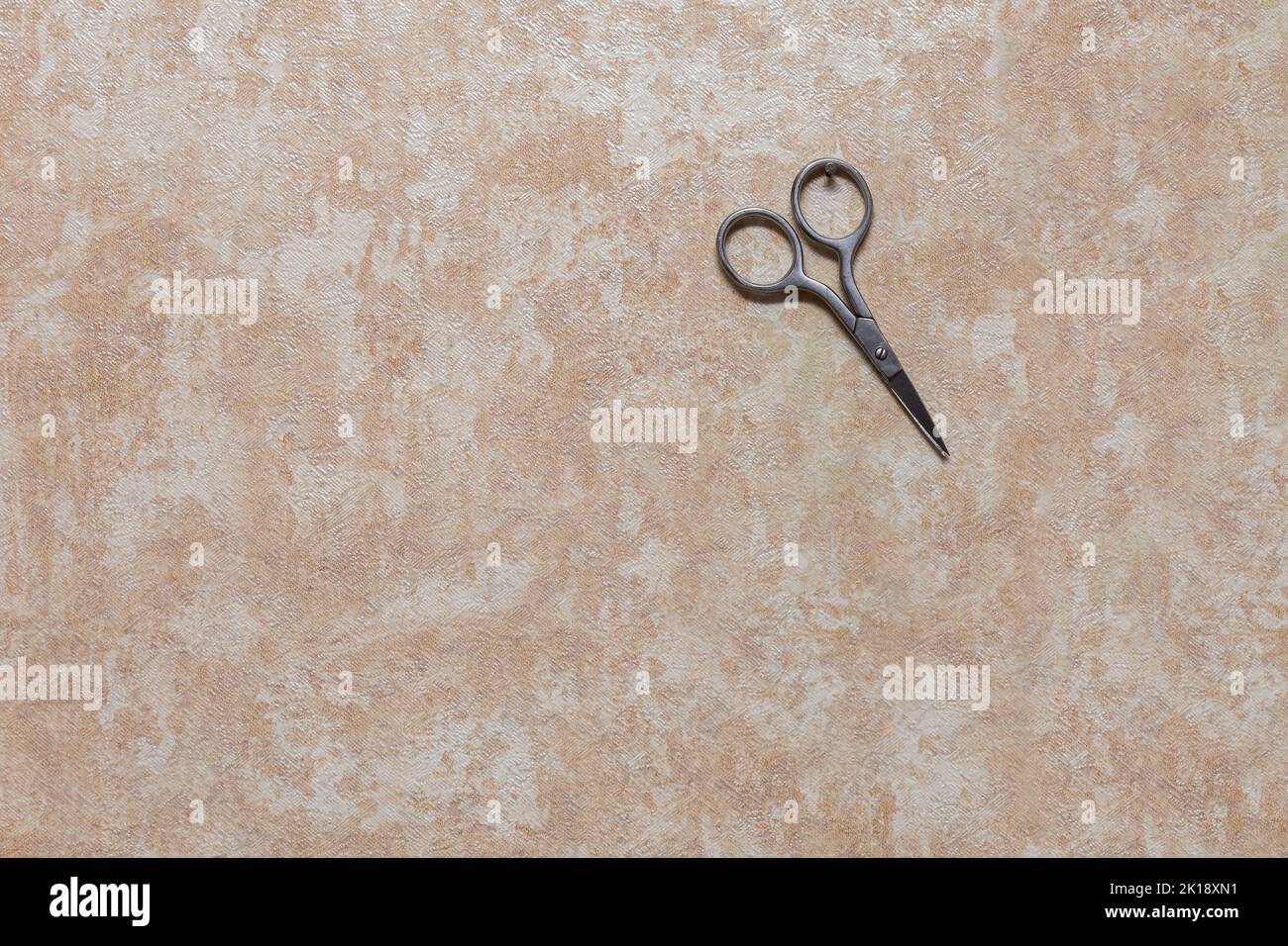 Manicure scissors hang on a small nail driven into the wall. Wall with wallpaper inside the house. Stock Photo