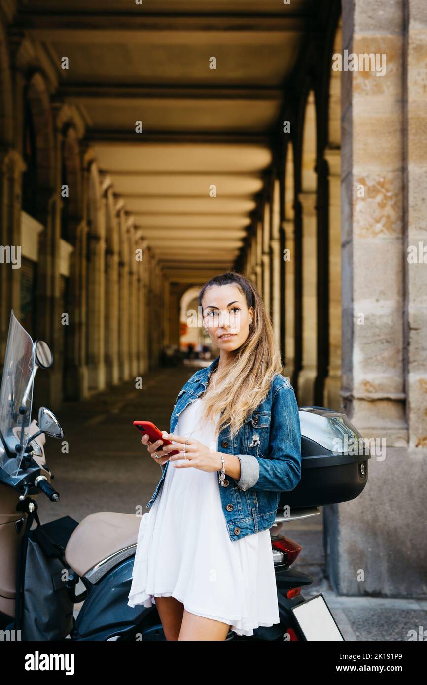 Young smiling woman on a motorbike using on a red smartphone Stock Photo