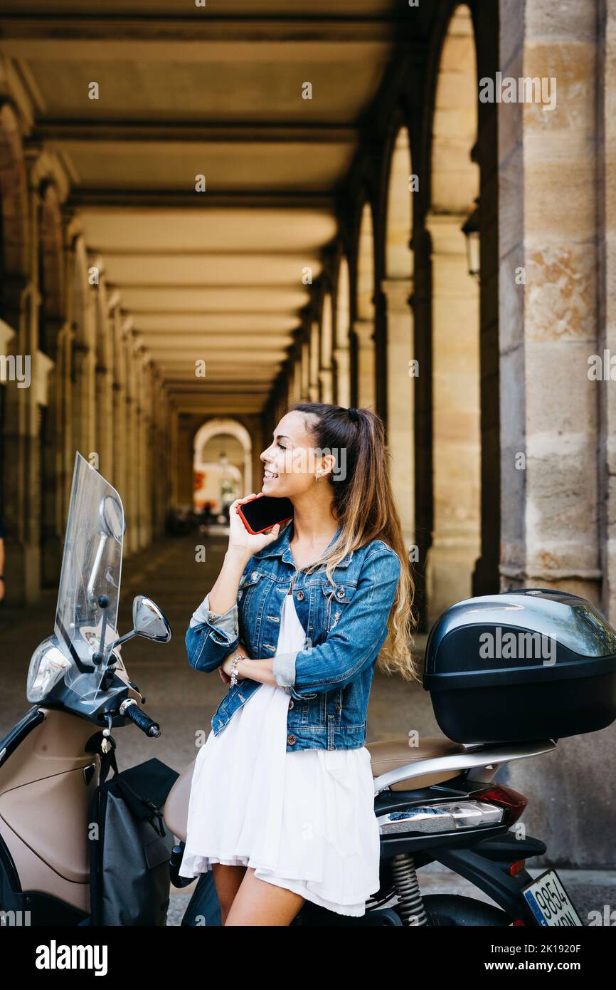 Young smiling woman on a motorbike talking on a red smartphone Stock Photo