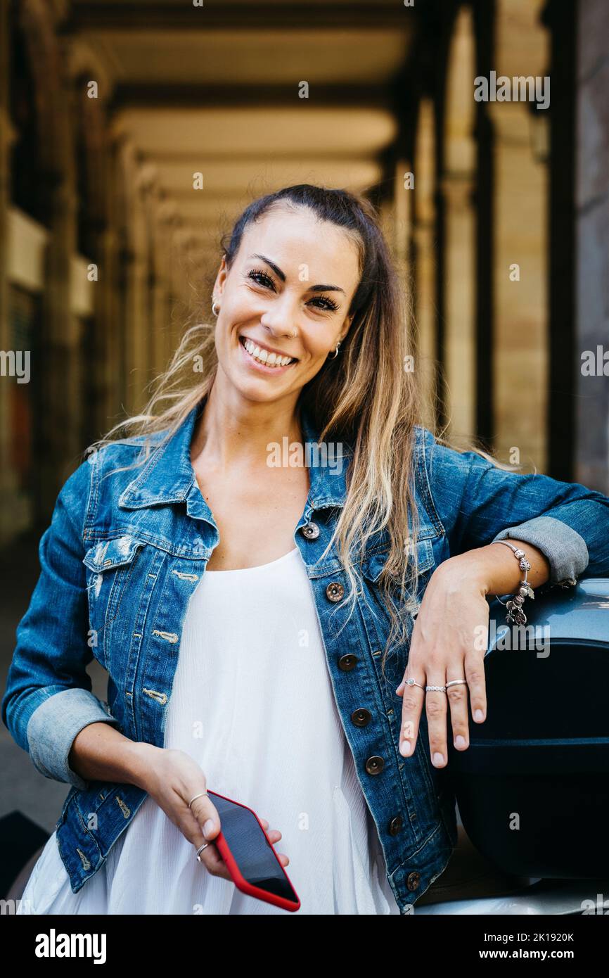 Portrait of a young smiling woman on a motorbike using on a red smartphone Stock Photo