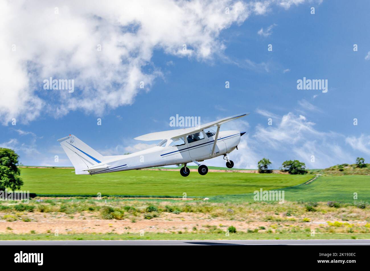 Single engine ultralight airplane taking off from airfield under blue sky with white clouds Stock Photo