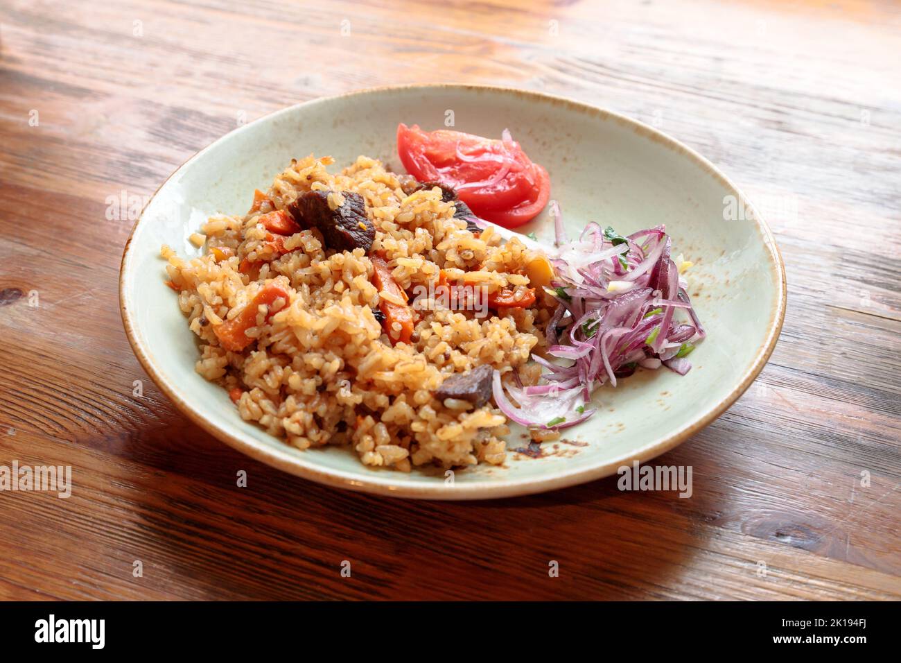 Pilaf with rice and beef or lamb and pickled red onion on a plate on a wooden background. Lifestyle Stock Photo