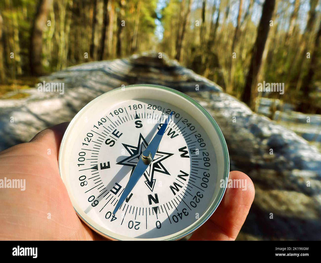 Spring calls for a journey. A forest road with melting snow and a tourist's hand with a compass, the arrow points north - follow the spring Stock Photo