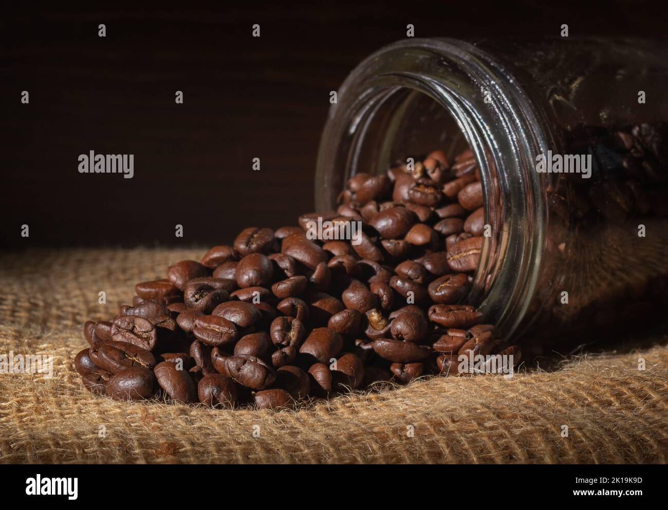Coffee beans spilled out of mason jar on burlap Stock Photo