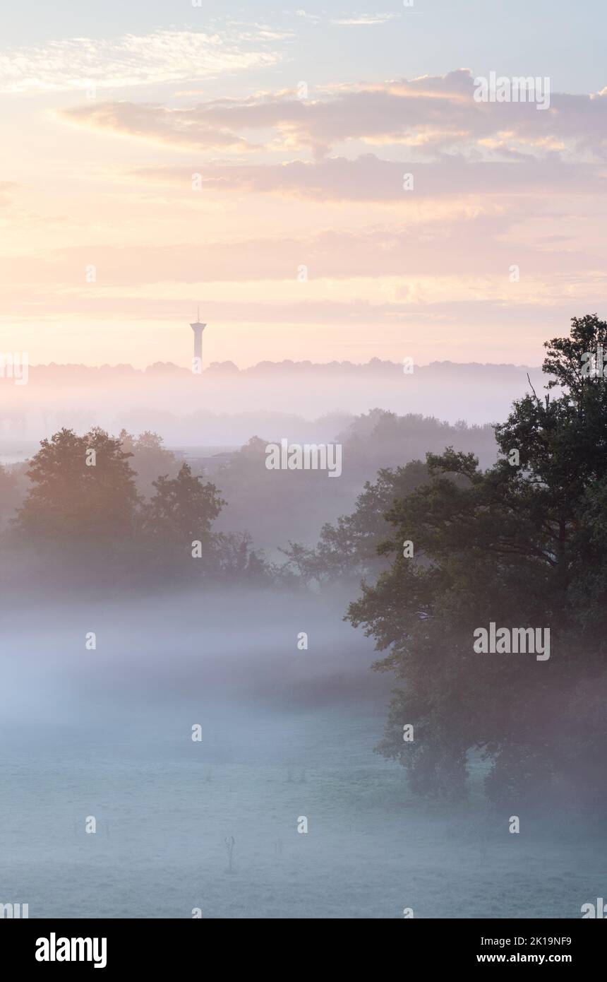 Morning mist creates pastel layers at sunrise in the rural landscape near Confolens in Poitou Charentes, with a water tower prominent on the horizon. Stock Photo
