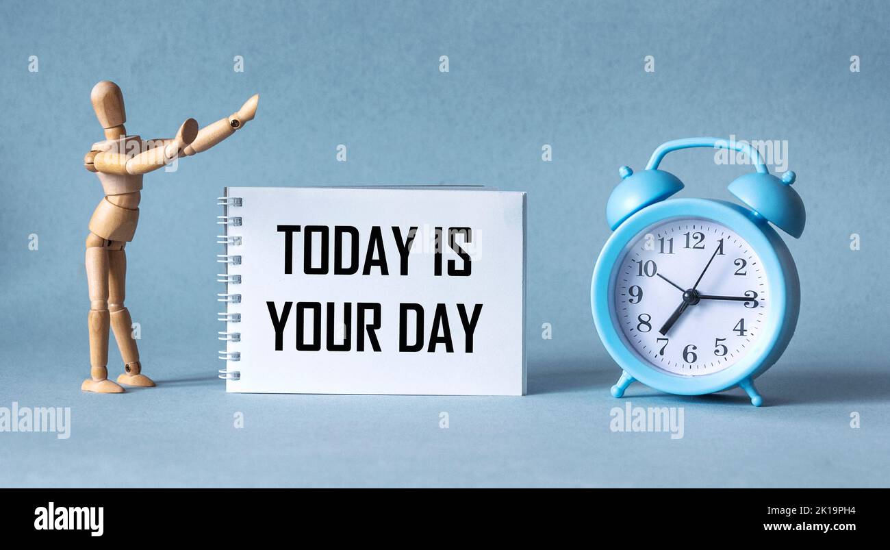 Alarm clock, wooden doll and notebook with the word Today is Your Day on a blue background Stock Photo