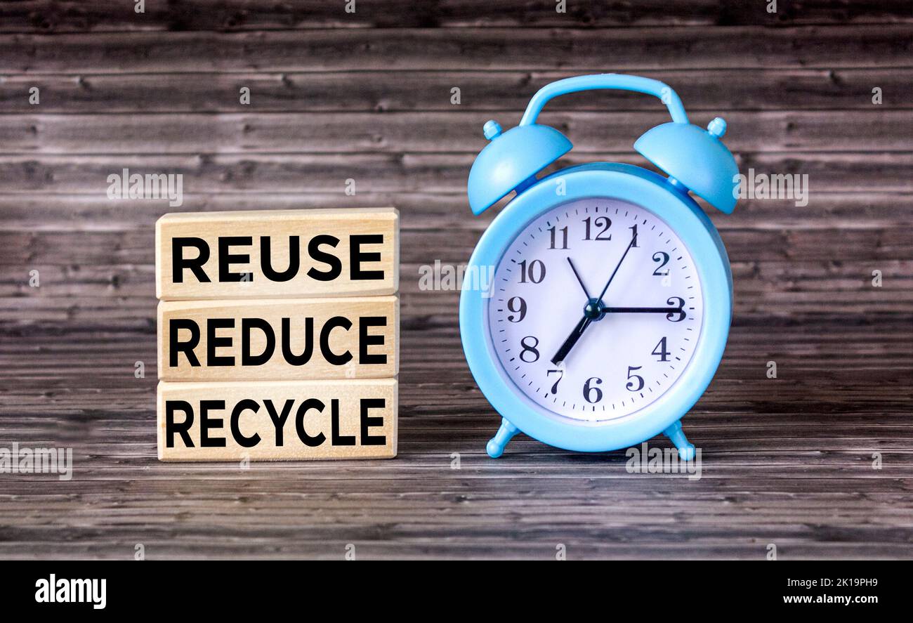 Environmental awareness and education concept. REUSE, REDUCE and RECYCLE written on wooden blocks with clock Stock Photo