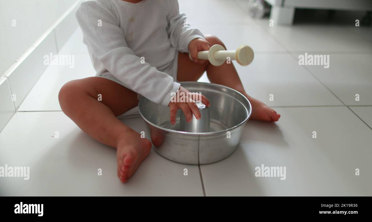 Baby on floor playing with kitchen utensils. One year old toddler