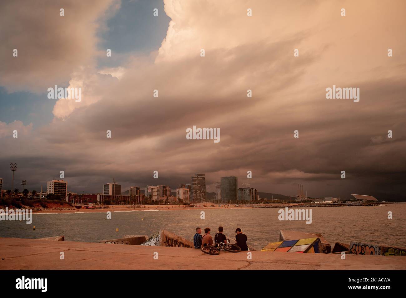September 16, 2022, Barcelona, Spain: A group of kids spend the afternoon on a breakwater as stormy clouds roll across the sky in Barcelona, Spain. Credit: Jordi Boixareu/Alamy Live News Stock Photo