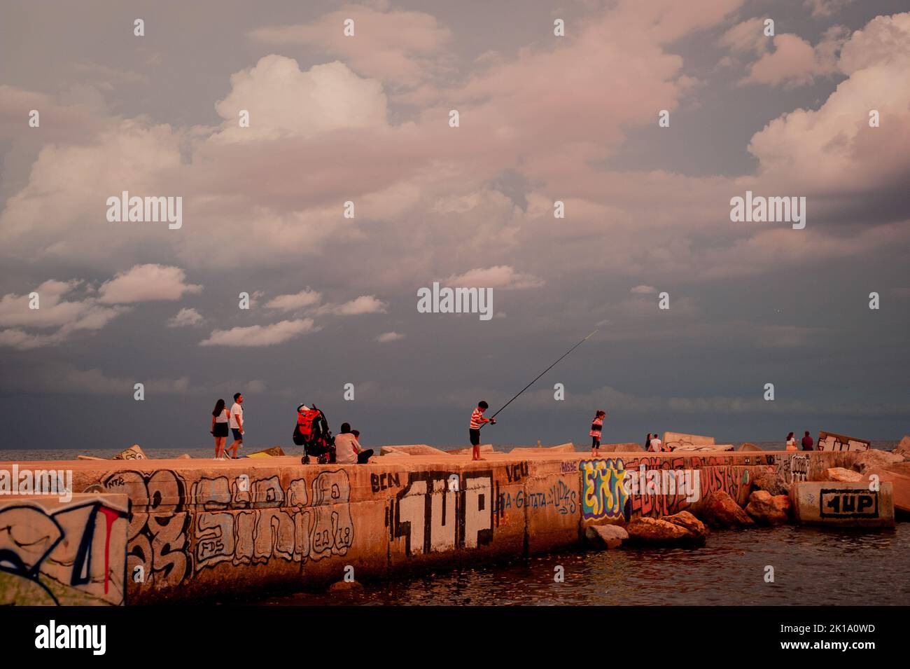 September 16, 2022, Barcelona, Spain: Young boy fishes from a breakwater as stormy clouds roll across the sky in Barcelona, Spain. Credit: Jordi Boixareu/Alamy Live News Stock Photo
