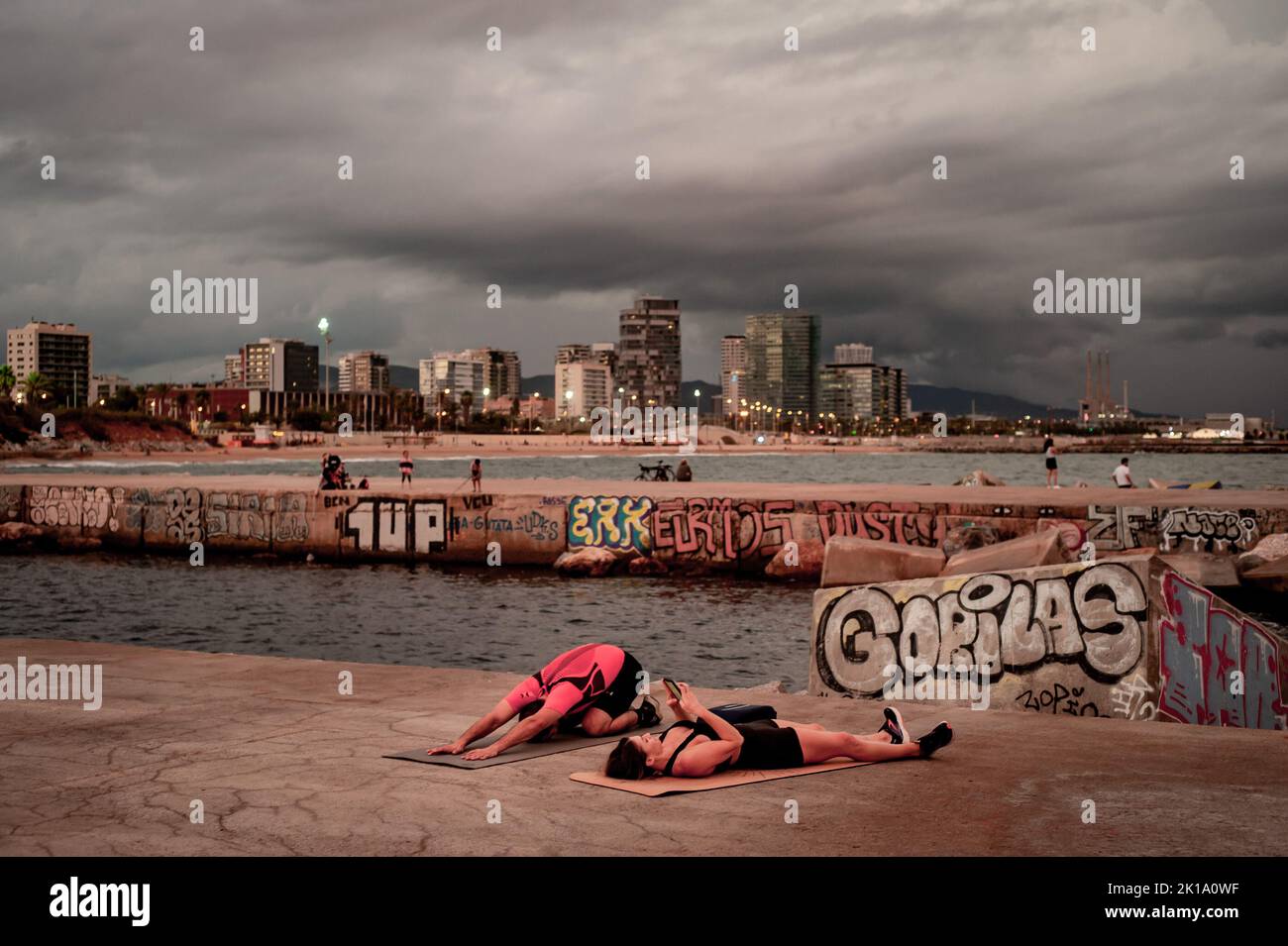 September 16, 2022, Barcelona, Spain: People exercise on a breakwater as stormy clouds roll across the sky in Barcelona, Spain. Credit: Jordi Boixareu/Alamy Live News Stock Photo