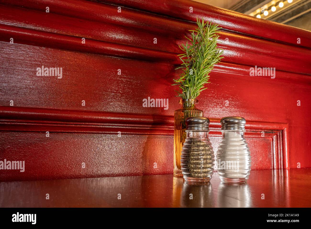 Tablescape background with red painted wall, salt, pepper, and vase with a bunch of live rosemary sitting on a wooden table. Red is used in restaurant Stock Photo