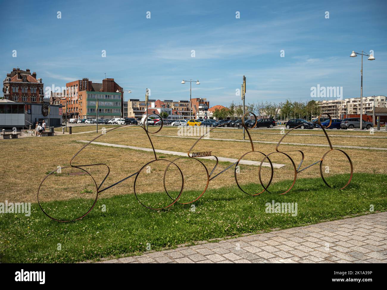 Europe, France, Dunkerque - July 9, 2022: Tour de France memorabilia. 3 rusted bicycle with rider profiles on green lawn of Place du Mynck under blue Stock Photo