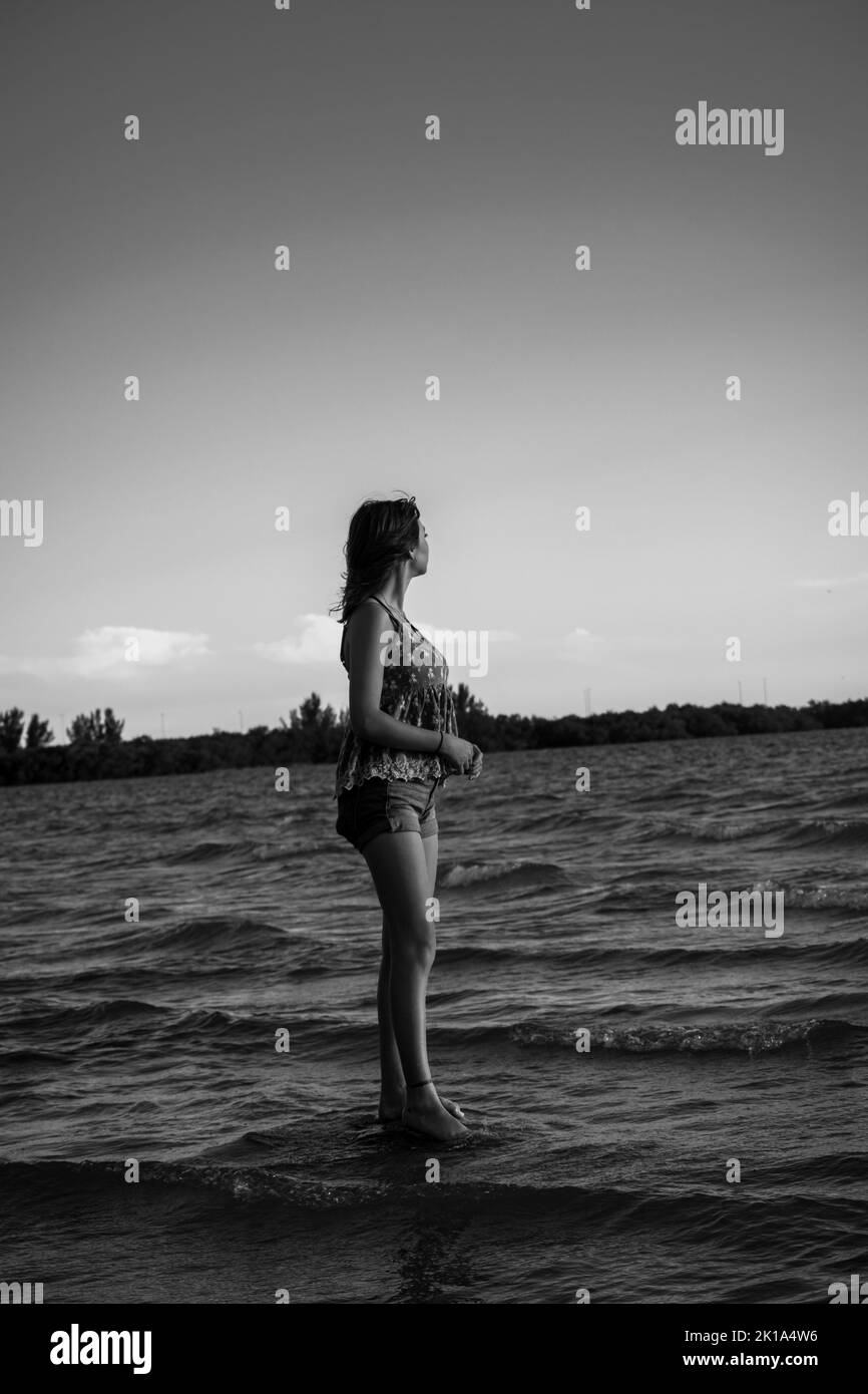 A vertical shot of a young female standing out on a rock and looking ...