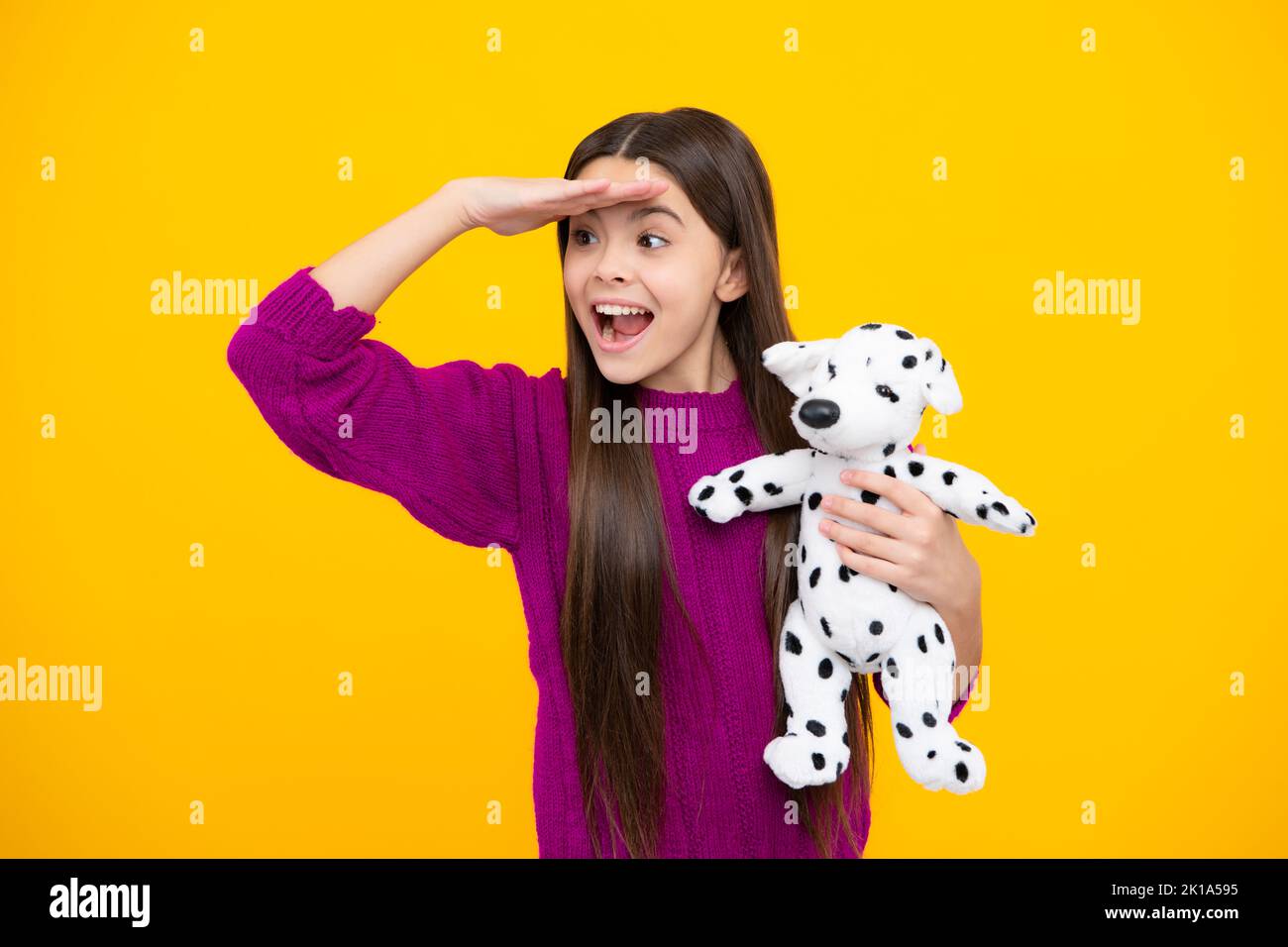 Excited face. Teen girl child in casual wear holding plush toy isolated on yellow background, happy childhood. Amazed expression, cheerful and glad. Stock Photo