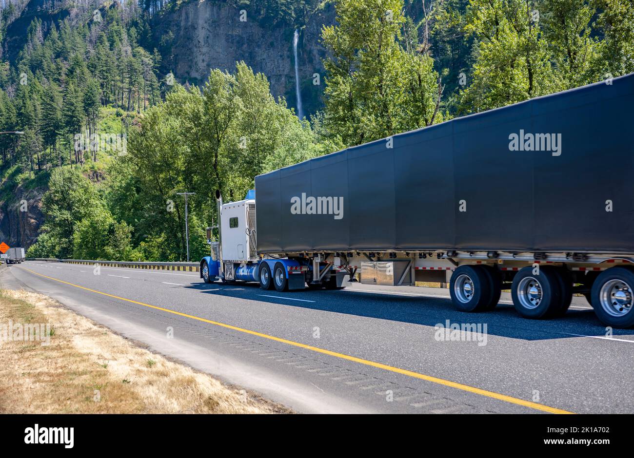 Industrial classic big rig white American semi truck tractor with cab sleeping compartment transporting cargo in dry van semi trailer driving on the r Stock Photo