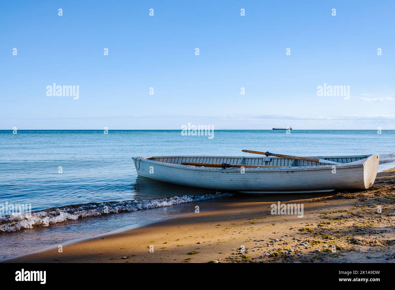 Old row boat on beach with shadow of trees. Calm ocean on the horizon. Stock Photo