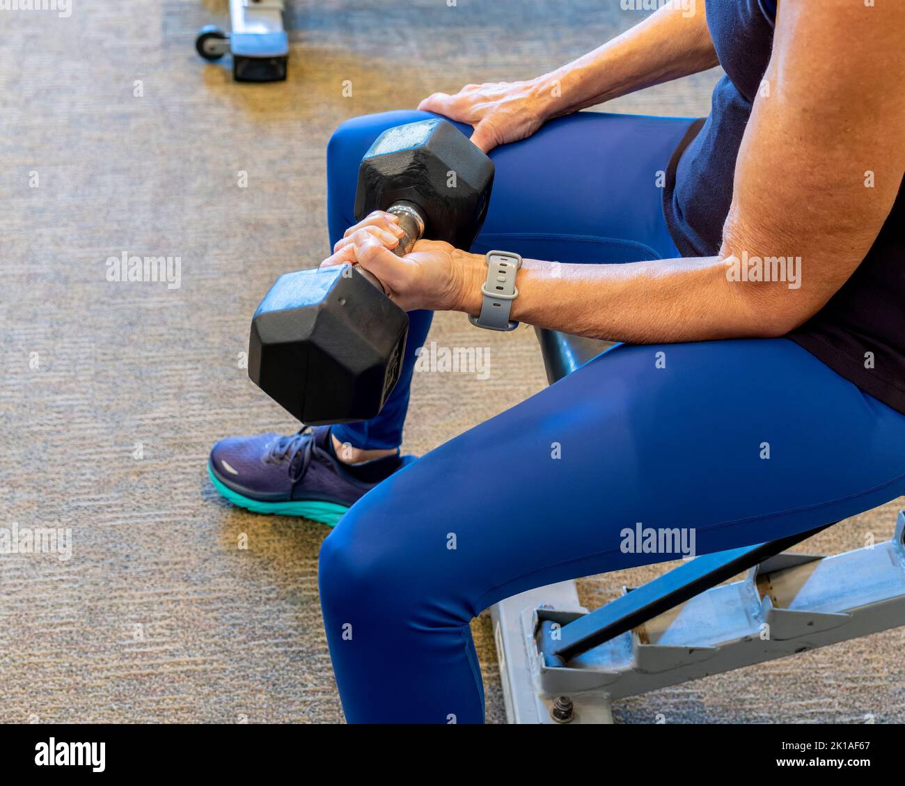 Middle aged mature or senior woman lifting weights or using weights or dumbbells in a gym for exercise, fitness and weight training. Stock Photo