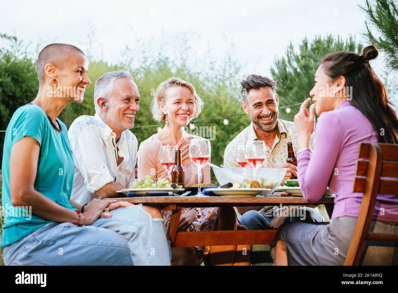 Group of adult friends or familly talking and having fun sitting at table in a dinner party in a back yard. Lifestyle concept. Stock Photo