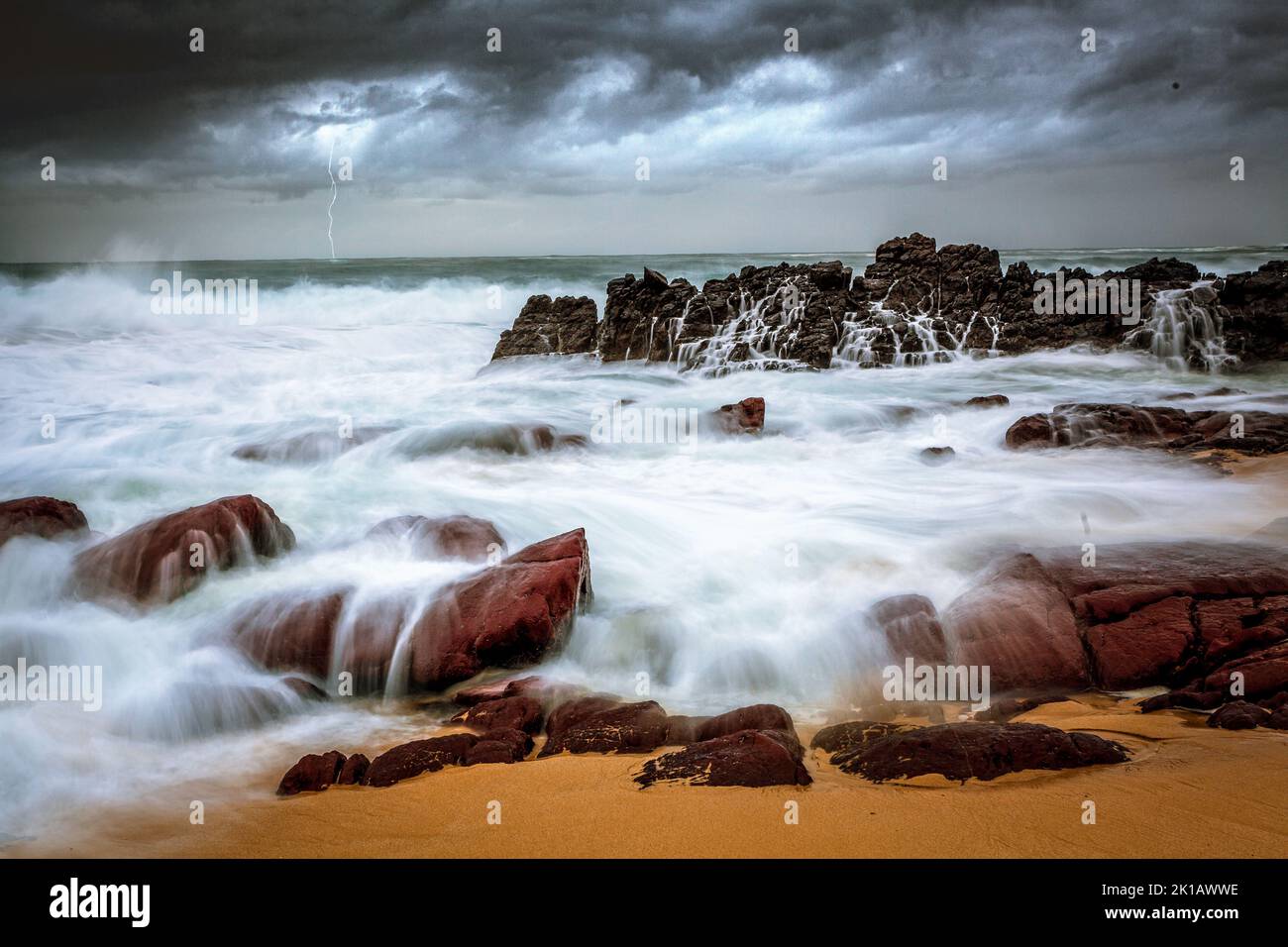 Storm over beach and turbulent waves crash over rocks onto seashore Stock Photo