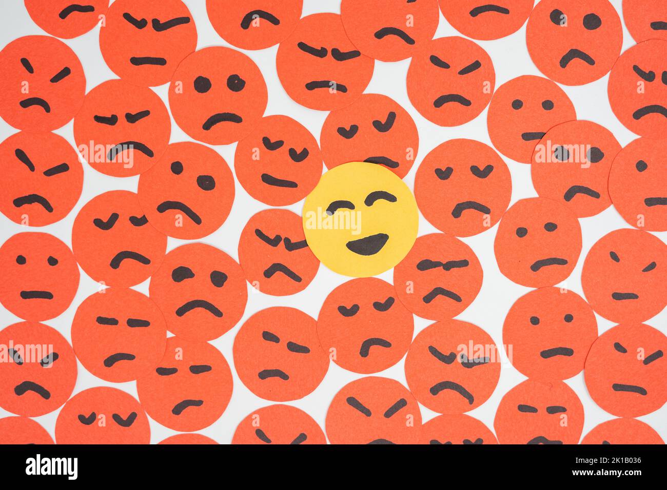 Concept for a positive attitude made with papers looking like sad faces with one that has smile and stands out Stock Photo