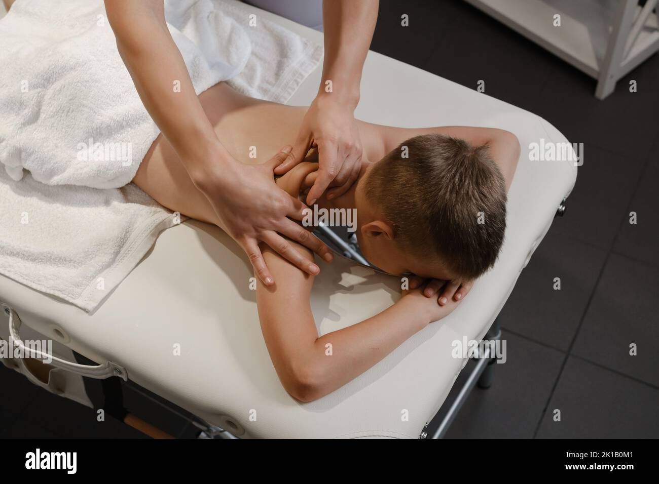 masseur gives the child a back massage. Kids massage concept. massage therapist giving 7 year old boy shoulder massage. Physical therapy Stock Photo