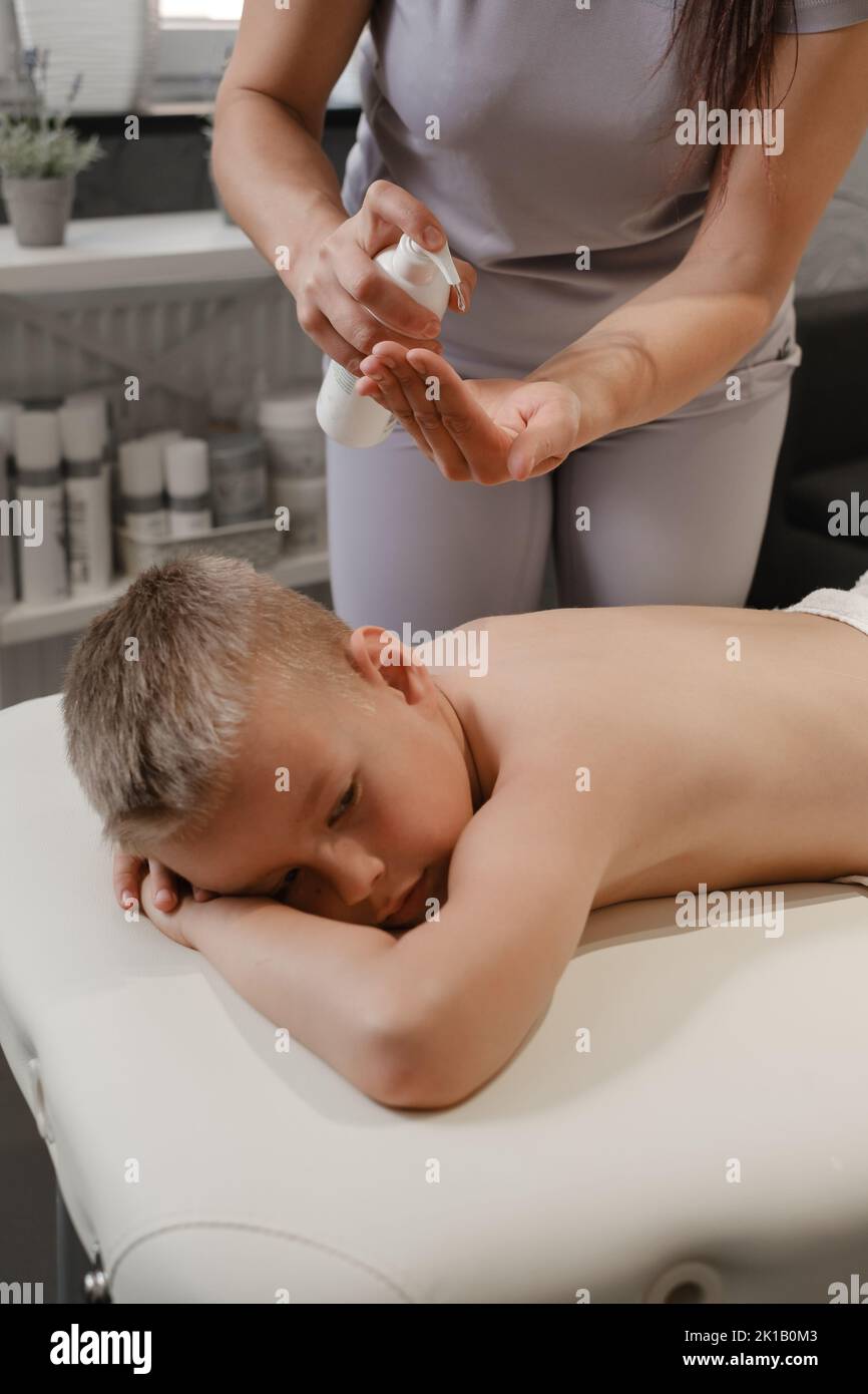 masseur hands pouring oil on child back. Masseuse prepare to do oriental spa procedure for relaxing treatment. Therapist doing aromatherapy oil Stock Photo