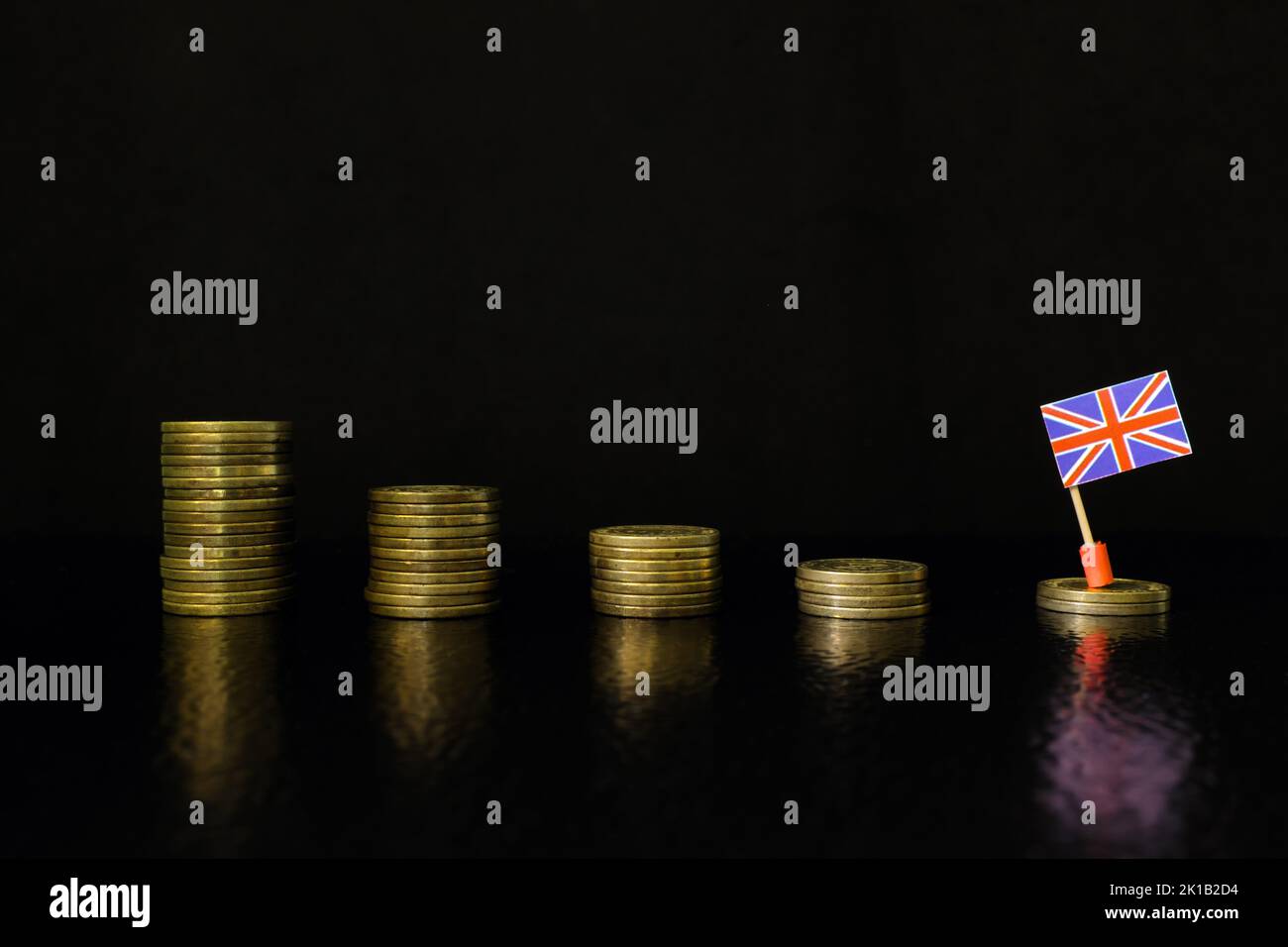 United Kingdom economic recession, financial crisis and currency depreciation concept. UK flag in decreasing stack of coins in dark black background. Stock Photo