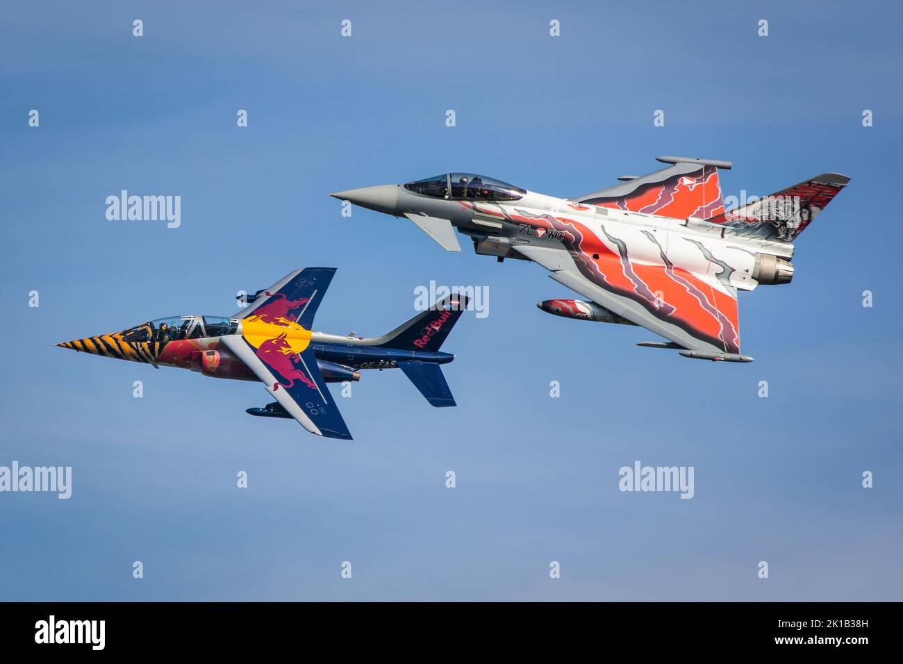 A Red Bull Alpha Jet and a Bundesheer Eurofighter Typhoon in special Tiger colors on a formation flight with blue sky Stock Photo
