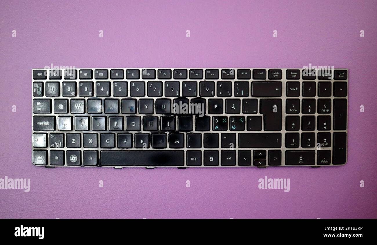 Heavily worn used broken laptop keyboard on purple background Stock Photo