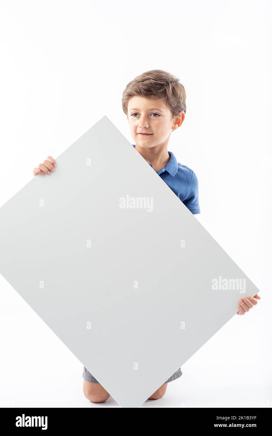 Funny Caucasian boy showing a white advertising poster with space for text, on a white background. Stock Photo