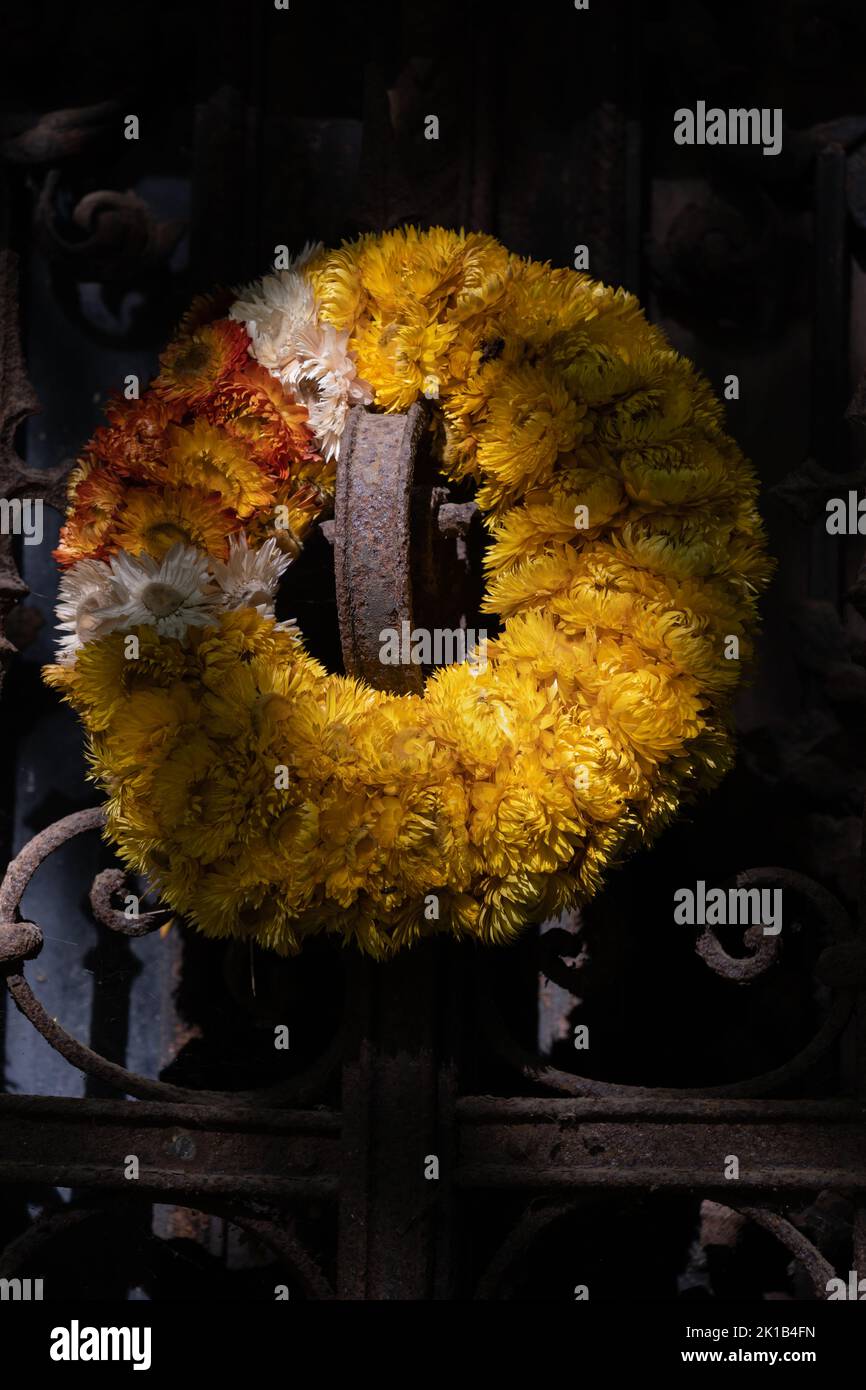 Old wreath in sunlight, made from dry flowers and put on tomb aged metal gate in cemetery. Stock Photo