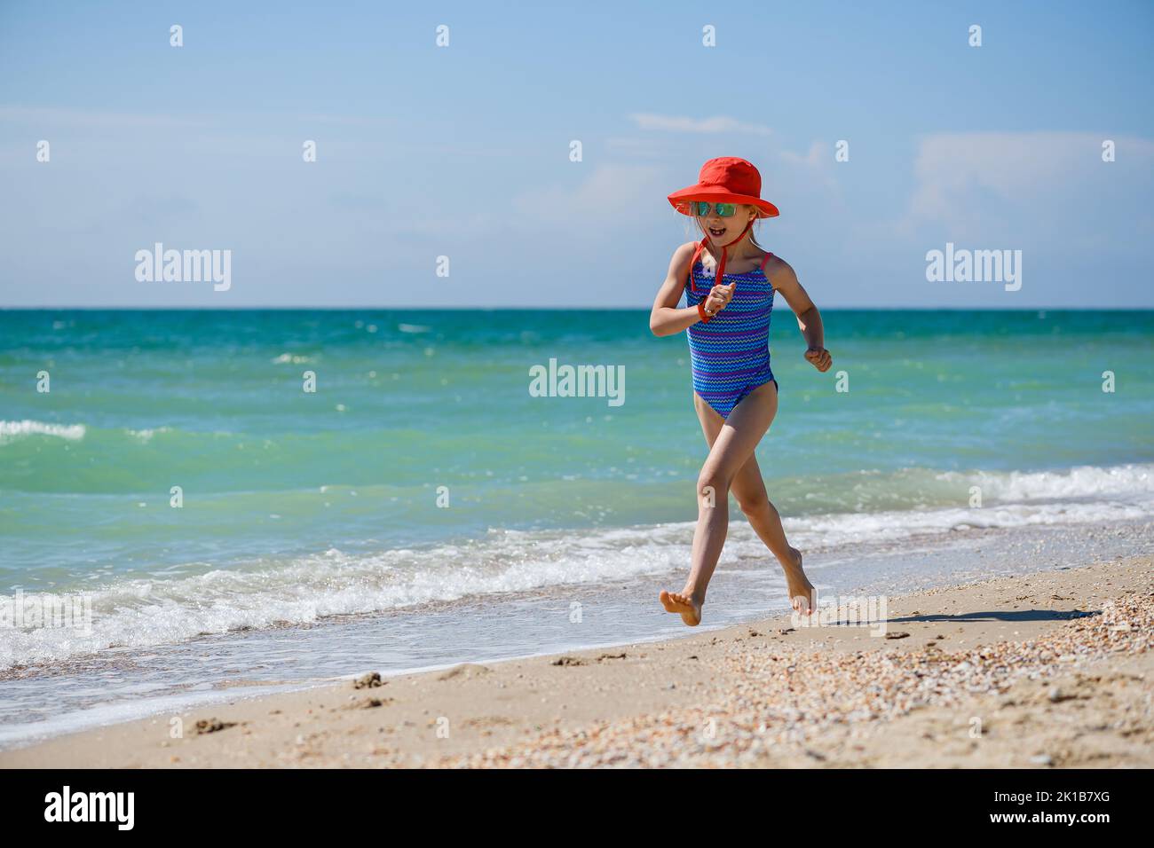 Little girl jogging running at sandy sea beach, wearing hat, sunglasses