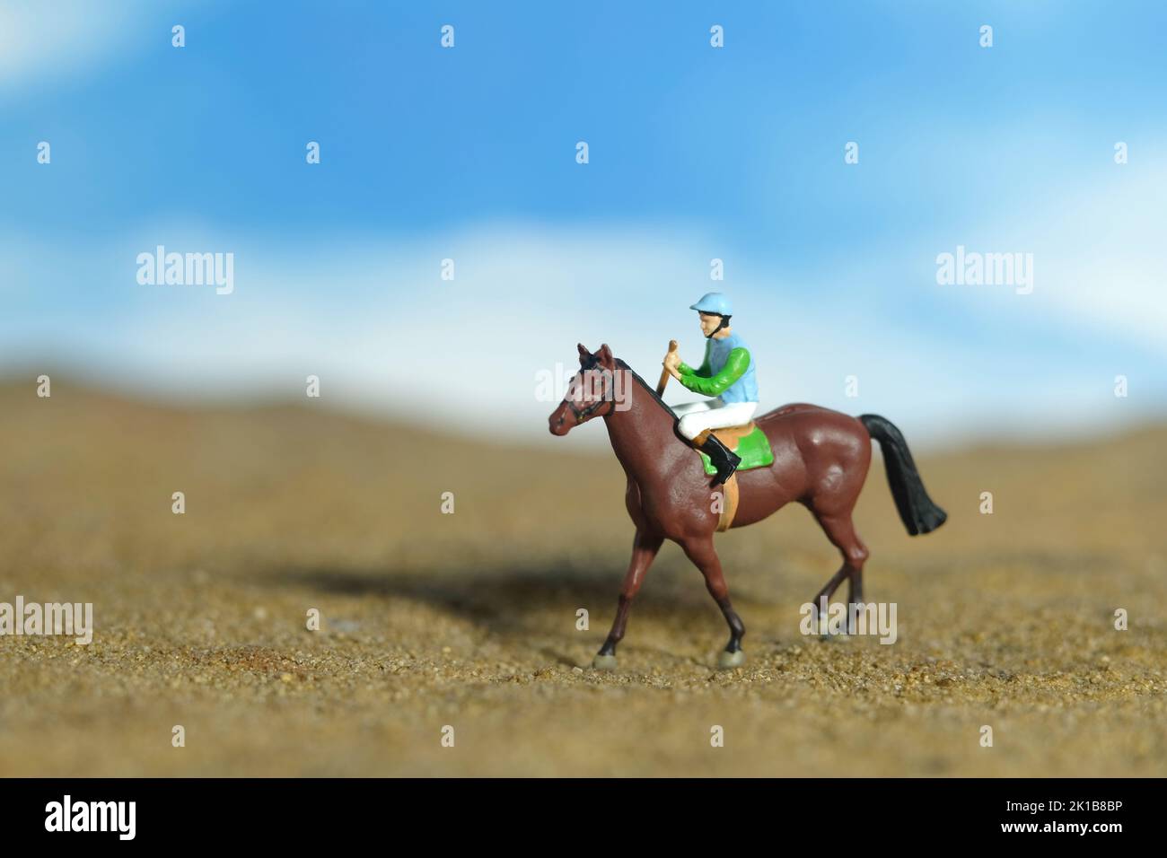 Miniature people toy figure photography. A jockey man riding horse at farm, sand desert land field. Image photo Stock Photo