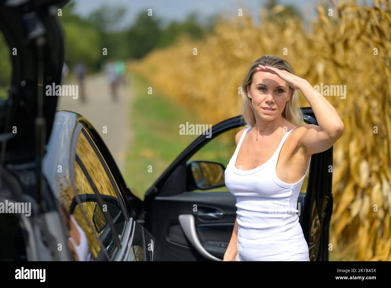 Woman standing by a car with a thoughtful look because of an car failure waiting for help with her to hand to the forehead Stock Photo