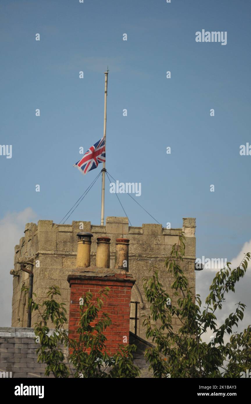 Church with flag half mast Queen Elizabeth death. Blue sunny summer sky and close up of church tower and chimney pots. Stock Photo