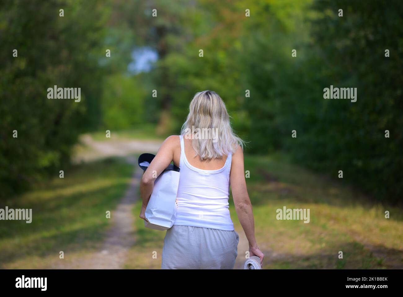 Rearview of an attractive blonde woman with a bag and a bath towel under her arm, on her way to or from the lake Stock Photo