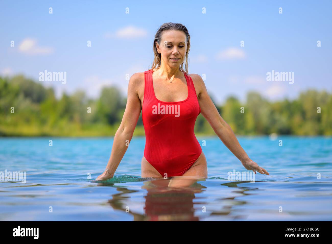 Gorgeous attractive blond woman with wet hair in a red swimsuit is slowly walking through the water with a smile Stock Photo