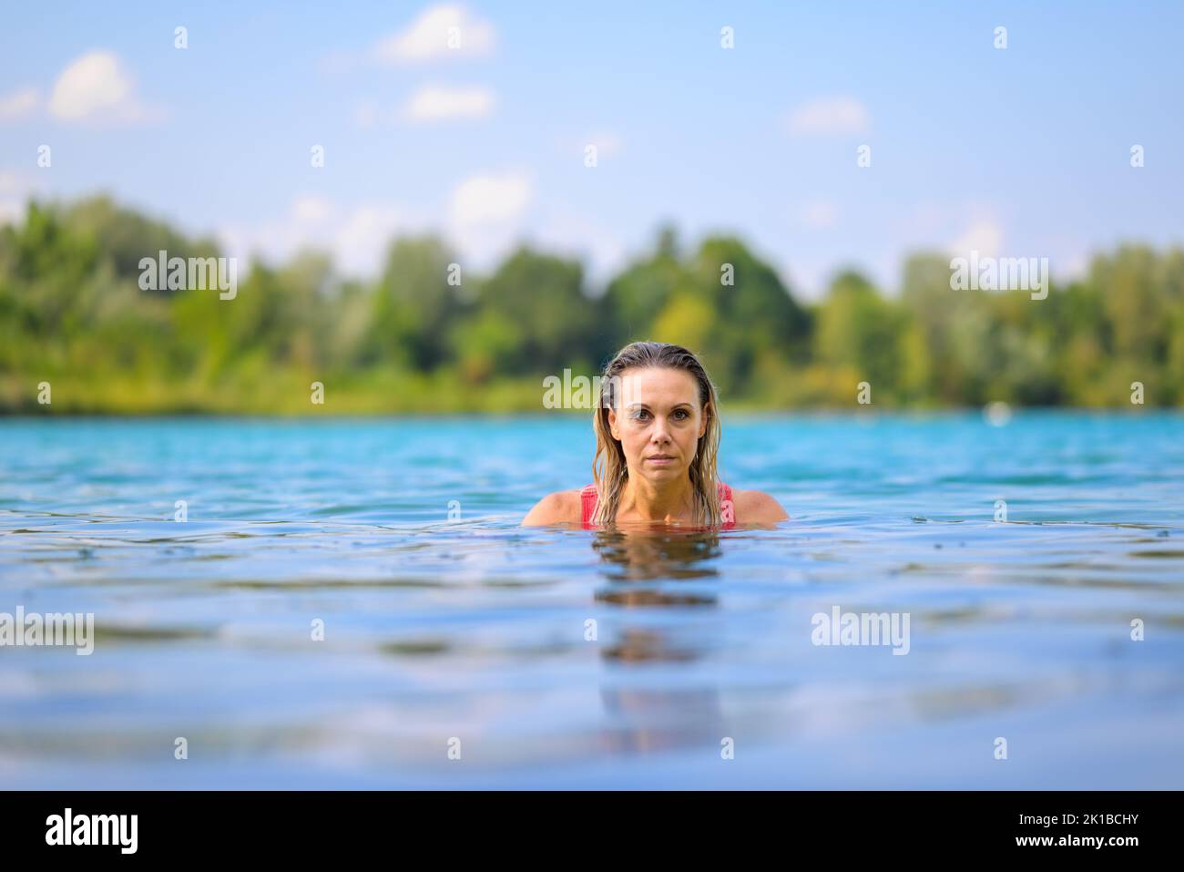 Gorgeous attractive blond woman with wet hair in a red swimsuit slowly rising out of the water with a stern look Stock Photo