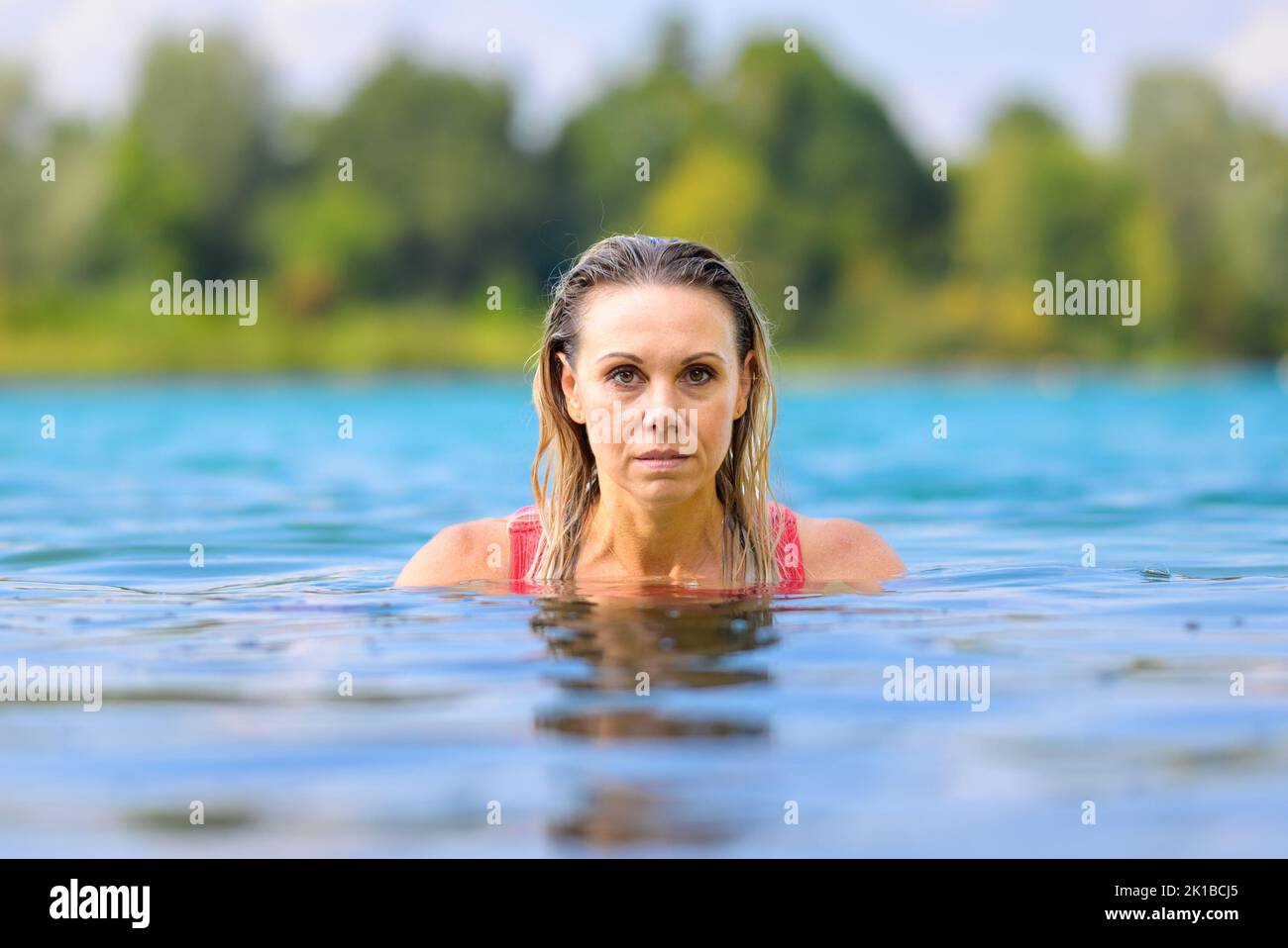 Gorgeous attractive blond woman with wet hair in a red swimsuit slowly rising out of the water with a stern look Stock Photo