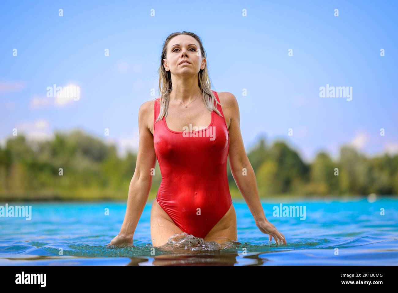 Gorgeous attractive blond woman with wet hair in a red swimsuit is slowly rising out of the water with a sensual look Stock Photo