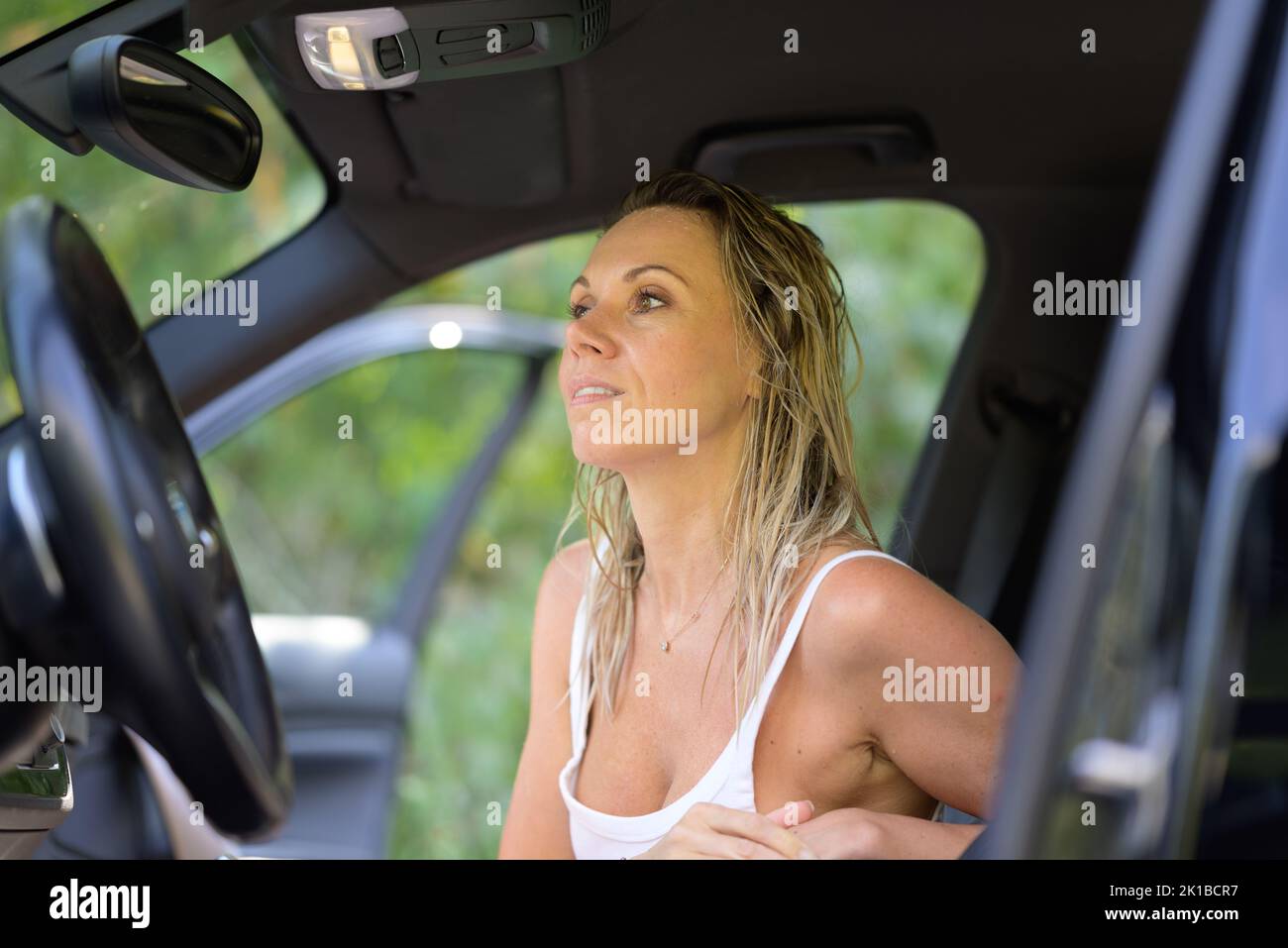 Woman with wet hair sitting in a car waiting with greenery in the background Stock Photo