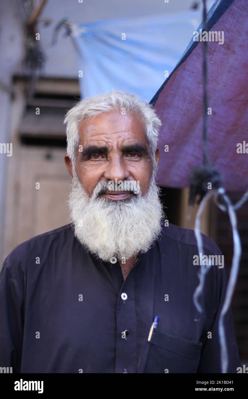 A vertical portrait of a Pakistani old male with a white beard in a kurta standing in the street Stock Photo