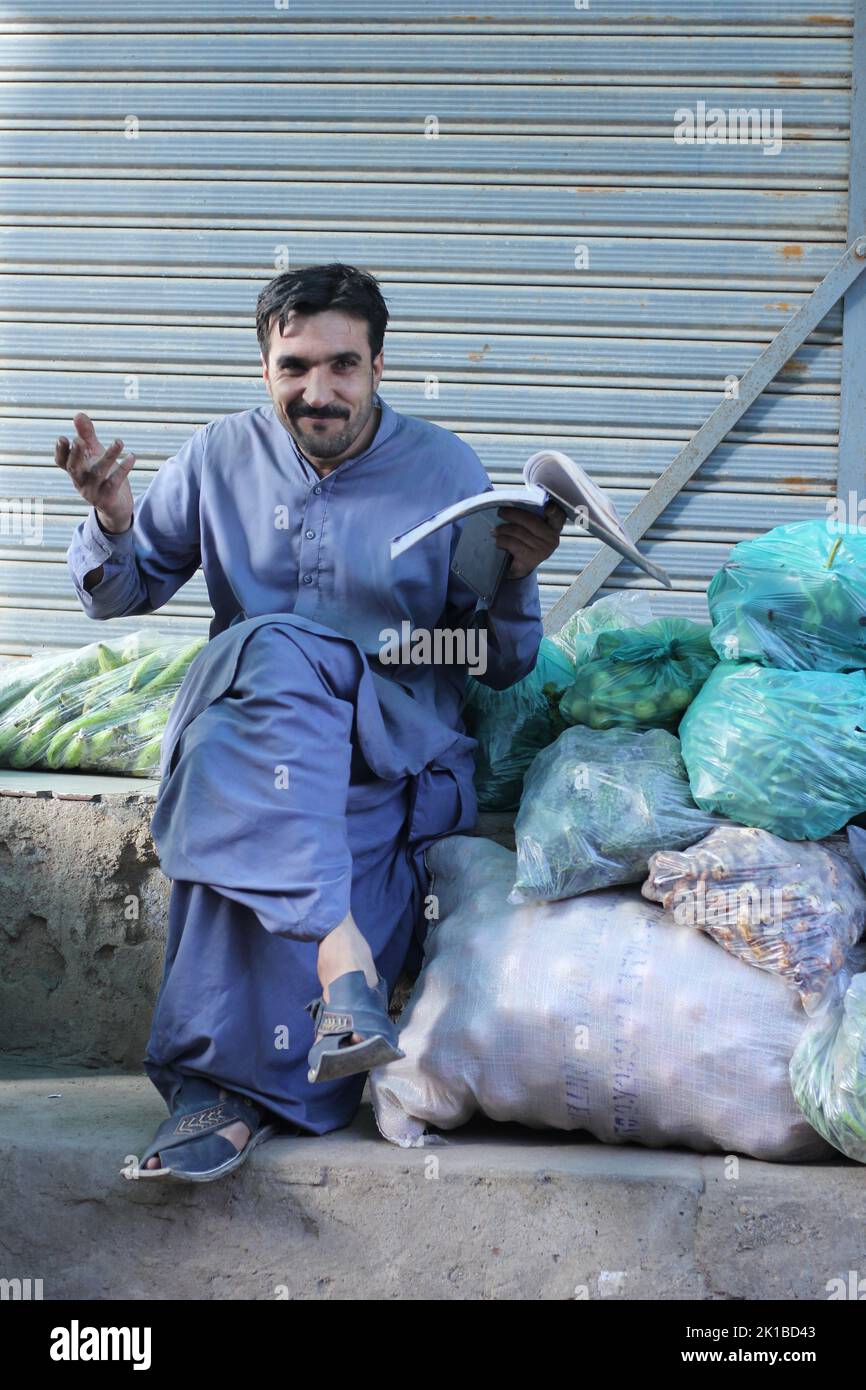 A vertical shot of a Pakistani male with mustache in a market selling fruits and reading book in shalwar kameez Stock Photo