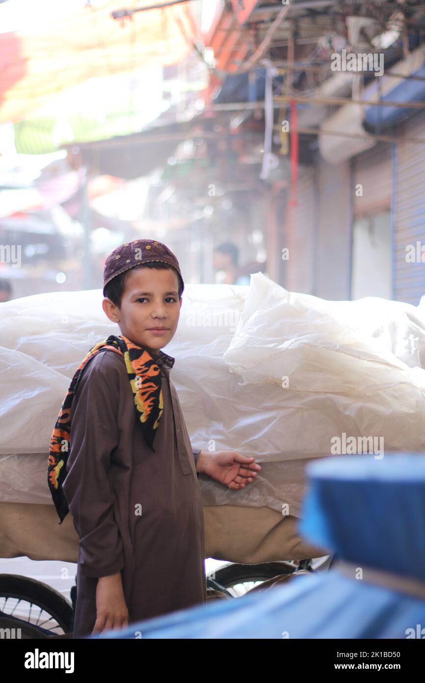 A vertical shot of a Pakistani young boy in a topi and kurta standing in the street Stock Photo