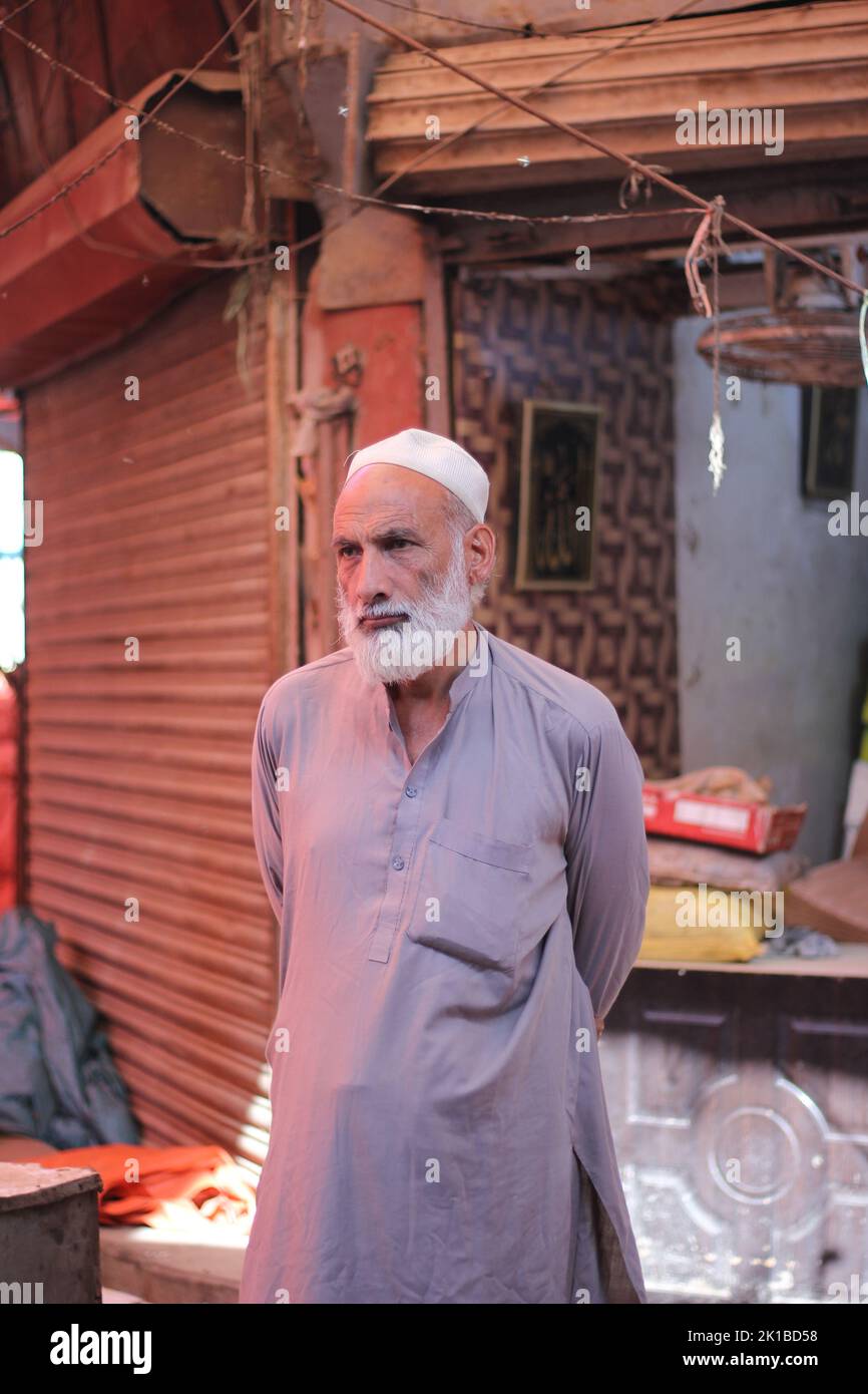 A vertical shot of a Pakistani old male with a white beard in a white topi and kurta on the street Stock Photo