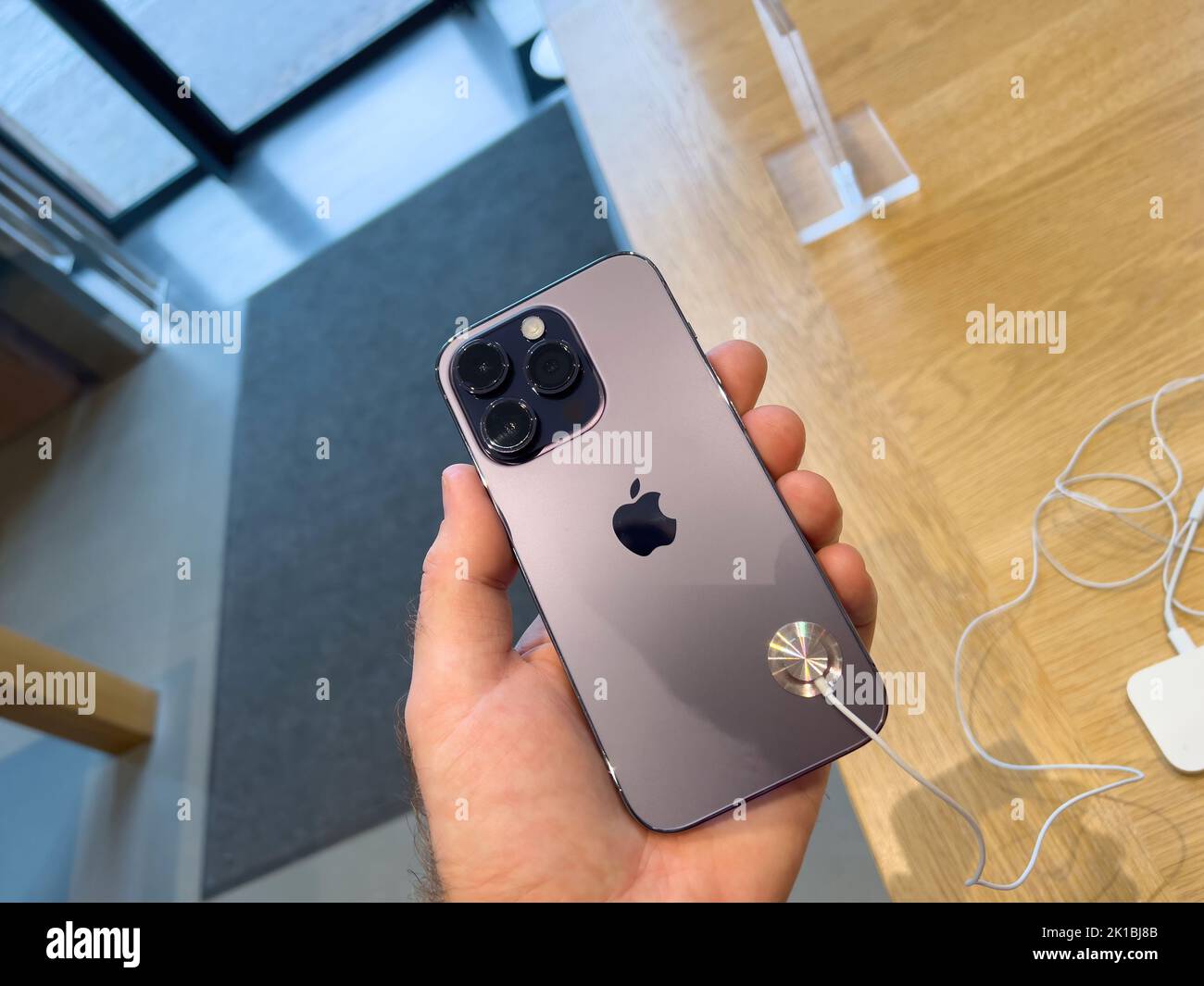 Paris, France - Sep 16, 2022: POV holding in hand new Apple Computers iPhone,14 Pro in deep purple on sale during the launch day featuring Always-on display, 48-megapixel camera and Dynamic Island - customers and genius workers in background Stock Photo