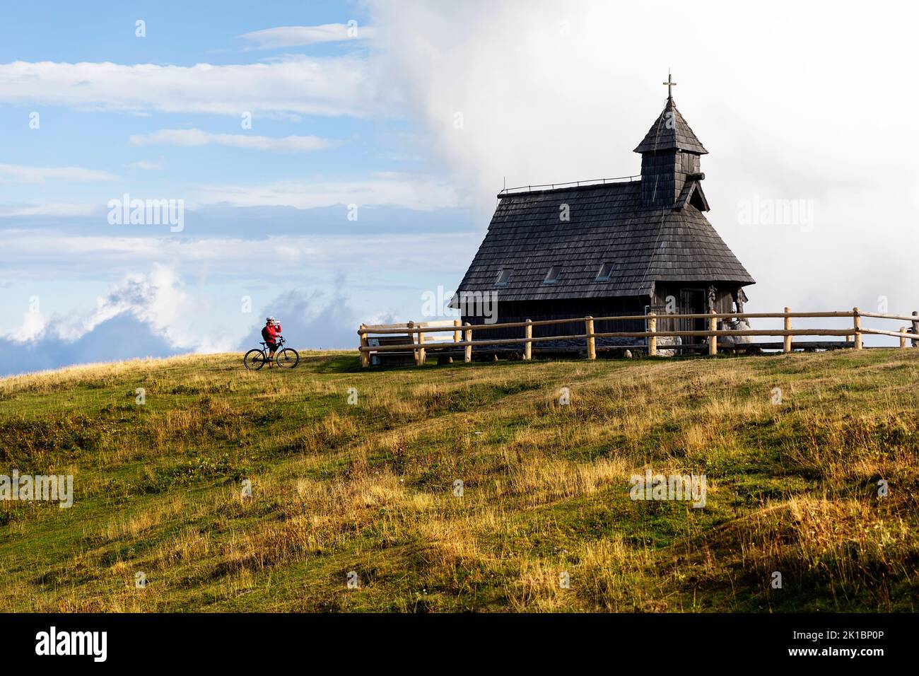 Woman tourist, cyclist on a trip to Chapel of Mary of the Snows located above shepherd's settlement on Velika planina alpine plateau, Kamnik, Slovenia Stock Photo
