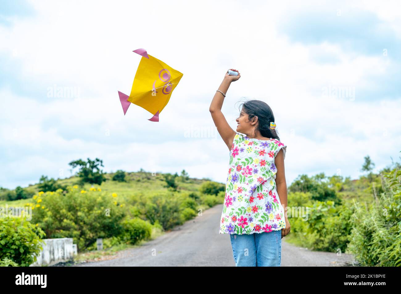 Excited happy girl kid running by flying kite during holidays - concept of holidays, playful vacation and carefree. Stock Photo