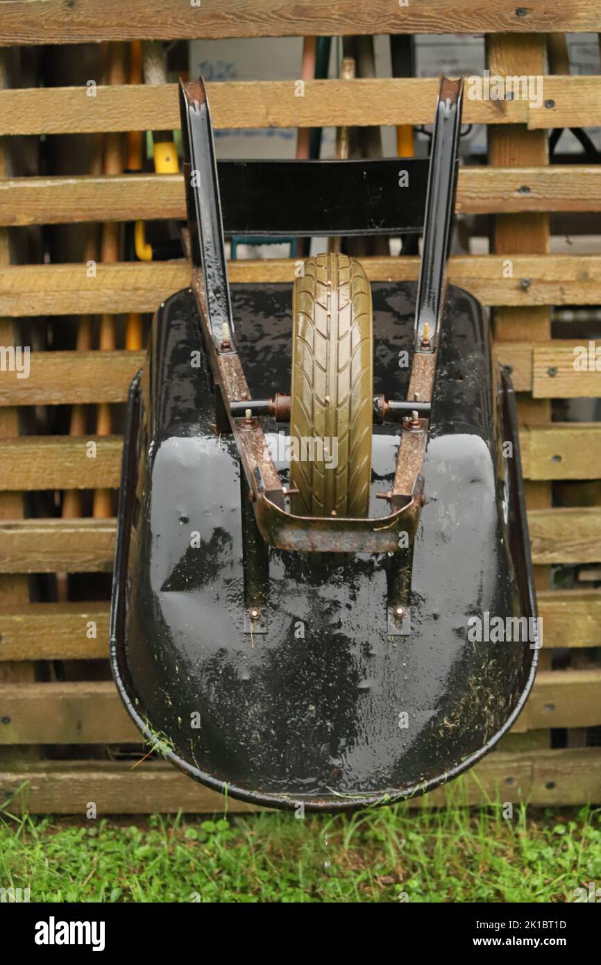 A vertical shot of a wet wheelbarrow hanging upside down at a garden pavilion while it is raining Stock Photo